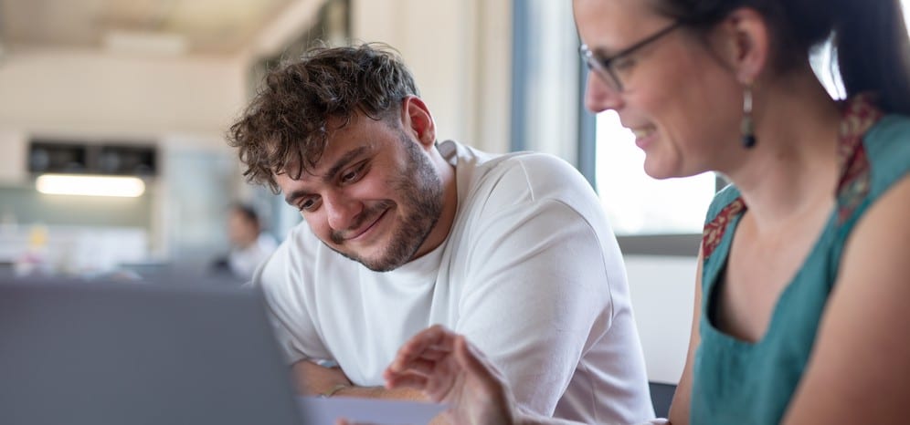 Un jeune homme et une collègue partagent un moment de travail devant un ordinateur, tout sourire, dans une structure engagée pour l'emploi inclusif.